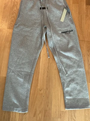 Grå Essentials mjukisbyxor - Säljer ett par grå essentials mjukisbyxor för att dom var för stora för mig tyvär. Dom är helt nya och oanvända.
