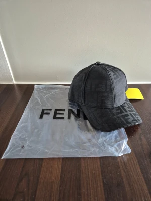 FF keps - Snygg svart keps från Fendi med deras ikoniska logomönster över hela kepsen. Klassisk böjd skärm och justerbar passform. Perfekt accessoar för att lyfta din streetwear-look.