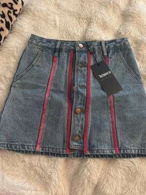 Jeanskjol med rosa detaljer - Snygg jeanskjol med knappar framtill och rosa detaljer. Helt ny med prislapp kvar