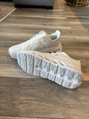 Vita On Cloud sneakers - Säljer ett par helvita On Cloud sneakers med ventilerande mesh-överdel och unika CloudTec-sulor för extra komfort. Skorna har en modern, sportig look med diskreta loggor på sidan och elastiska snören för enkel påtagning. Kartong ingår 