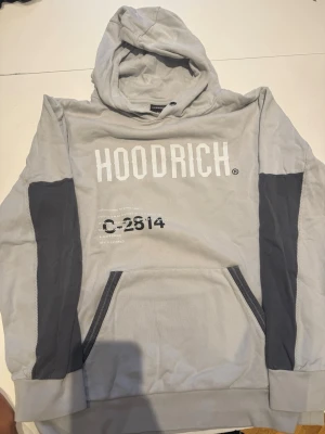 Grå hoodie från Hoodrich XL - Snygg grå hoodie från Hoodrich med vita tryck på bröstet och svarta detaljer på ärmar och fickor. 