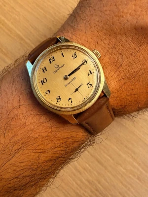 Certina Bristol 228 guldplaterad klocka - Stilren Certina Bristol 228 med ”brushed gold” urtavla och klassiska breguet siffror. Klockan har ett runt boett i metall och ett brunt läderarmband som ger en tidlös look. Perfekt accessoar för dig som gillar vintagevibbar och snygg design.