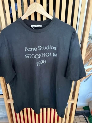 Svart Acne Studios t-shirt - Cool svart t-shirt från Acne Studios med trycket 'Acne Studios STOCKHOLM 1996' på bröstet. Klassisk rund hals och korta ärmar. Perfekt basplagg med street vibe och enkel stil. Tillverkad i mjuk bomull för skön känsla.Storlek L och i oanvänt skick. 