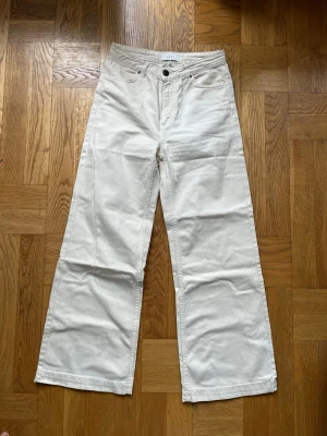 Vida vita jeans med hög midja - Säljer ett par vita jeans med hög midja och vida ben. Klassisk femficksmodell med knapp och dragkedja framtill. Jeansen har raka, breda ben och är tillverkade i ett kraftigare bomullstyg. Storlek 27!! 