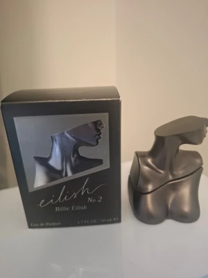 Eilish No.2 parfym Billie Eilish - Eilish No.2 Eau de Parfum från Billie Eilish i en unik, skulptural flaska som liknar en metallisk byst i mörkgrått. Flaskan har en modern och konstnärlig design som sticker ut på parfymhyllan. Innehåller 50 ml doft.