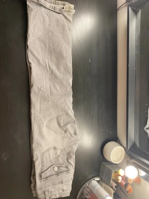 Gråa raka jeans med fickdetalj - Snygga grå jeans med rak passform och en bakficka med lock och knapp. Jeansen har klassisk design och är tillverkade i denim. Perfekta för en avslappnad och trendig look.