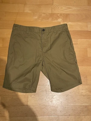 Beiga shorts med normal passform - Snygga beiga shorts i bomull med normal passform. Klassisk design med knapp och dragkedja framtill samt bälteshällor. Perfekta för varma dagar och enkla att matcha med olika stilar.