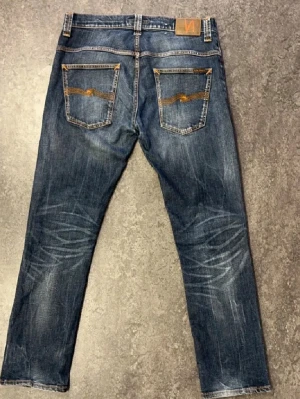 Nudie Jeans med fett sjuk wash, W34, L32 - Säljer ett par blå Nudie jeans med slitningar och lagade detaljer på benen. Jeansen har raka ben, klassisk femficksmodell och kontrastsömmar. Otroligt sjuk wash. De är även lagade 