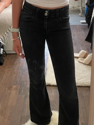 Svarta bootcut jeans med hög midja - Säljer ett par svarta bootcut jeans med hög midja och dubbla knappar framtill. Jeansen har klassiska fem fickor och är i stretchigt denimtyg som sitter snyggt. Perfekta till en enkel topp eller hoodie.