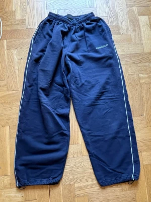 Mörkblåa Iets Frans byxor från Urban Outfitters - Navy Harri Baggy Joggers från Urban Outfitters med vita stripes längs sidorna och broderad Iets Frans logga på vänster sida. Byxorna har resår i midjan och dragsko vid bensluten. I gott skick men lite urtvättade, därav det låga priset. 