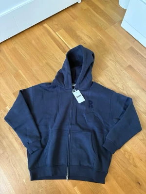 DARK BLUE RISKY PLAINZ ZIP HOODIE Nypris 663 kr - Säljer en DARK BLUE RISKY PLAINZ ZIP HOODIE helt ny och kommer med tagsen. Mörkblå hoodie från Risky med hel dragkedja framtill och stor huva. Hoodien har en broderad 'R' på bröstet och rymliga fickor framtill. Tillverkad i mjuk bomull och har en relaxed passform som passar perfekt till en chill stil. Nypris 663 kr 
