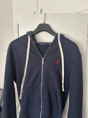Marinblå hoodie från Polo Ralph Lauren - Snygg marinblå hoodie med dragkedja från Polo Ralph Lauren. Hyfsat ny hoodie knappt använd, Det är M men passar även för det som har S vanligtvis, den är för liten för mig då jag är över 190.