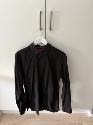 Svart skjorta från HUGO Boss - Stilren svart skjorta från HUGO med klassisk svart färg som passar till allt! Skjortan är i storlek 44 som visas på bild. 
