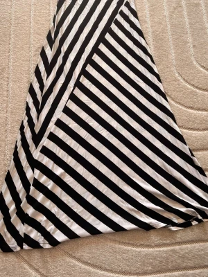 Svartvit klänning med ränder - Säljer en svartvit klänning ju med breda diagonala ränder. Kjolen har en flowy passform och är tillverkad i ett mjukt, lätt tyg som känns skönt mot huden. Perfekt för dig som gillar grafiska mönster och vill sticka ut lite extra.