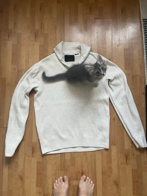 Beige stickad tröja från Jack & Jones - Snygg beige stickad tröja från Jack & Jones med hög krage och dragkedja. Tröjan har lång ärm och är tillverkad i mjukt material som passar perfekt för lager på lager. Enkel och stilren design som funkar till det mesta.