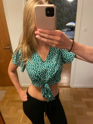 Grön blommig topp - Grön croppad topp med vita små blommor och knyt framtill. Toppen har v-ringning och korta, fladdriga ärmar. 