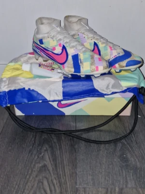 Nike Mercurial Elite fotbollsskor SoCal pack - Säljer ett par Nike Mercurial fotbollsskor med högt skaft och färgglatt mönster i blått, rosa, gult och vitt. Skorna är i bra skick bara att de är smutsiga.                     Allt på bilden medföljer. Kontakta gärna ifall du har frågor
