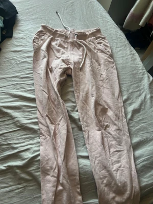 Ljusrosa mjukisbyxor från 157 XS - Ljusrosa mjukisbyxor från 157 med dragsko i midjan och ribbade muddar. Byxorna har två fickor fram och är gjorda i ett mjukt och bekvämt material, perfekta för chill dagar. Passar dig som gillar en avslappnad och enkel stil.