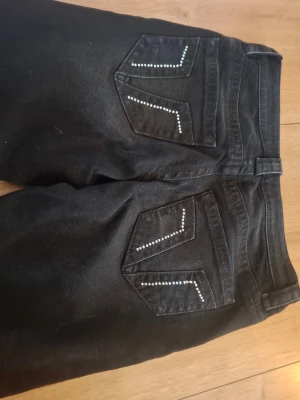 Svarta jeans med nitar från Gina Tricot - Snygga svarta jeans från Gina Tricot med dekorativa nitar på bakfickorna. Jeansen har klassisk femficksmodell och raka ben. Materialet är stretchigt för extra komfort. Perfekta för dig som vill ha en cool och trendig look.
