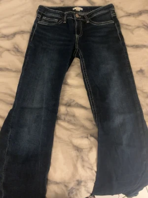 Mörkblå bootcut jeans - Säljer ett par mörkblå bootcut jeans med vita snygga detaljer på bakfickorna. helt oanvända. storlek 164