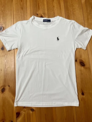 Vit t-shirt från Polo Ralph Lauren - Klassisk vit t-shirt från Polo Ralph Lauren med liten broderad logga på bröstet. T-shirten har rund halsringning och korta ärmar. Tillverkad i mjuk bomull för en skön känsla och stilren look.