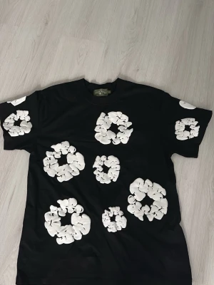 Svart t-shirt med vita blommor - Cool svart t-shirt med stora vita blommor tryckta över hela plagget. T-shirten har rund hals och korta ärmar, perfekt för en avslappnad och trendig stil. Materialet känns mjukt och bekvämt mot huden. Startpris är 500kr