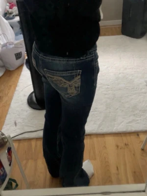 Mörkblå bootcut jeans med brodyr - Säljer ett par mörkblå bootcut jeans med snygg broderad detalj på bakfickorna. Jeansen har kontrastsömmar och klassisk femficksmodell. Materialet är denim med lätt stretch för skön passform. Perfekta för dig som gillar en avslappnad men trendig look.