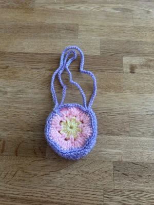 Virkad snusväska  - Söt snusväska i virkat material med lila, ljusrosa och gula toner. Väskan har ett blommigt mönster. Perfekt accessoar för dig som gillar boho och unika detaljer.