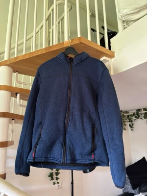 Mörkblå fleecejacka med dragkedja - Mysig mörkblå fleecejacka med hel dragkedja framtill och två fickor med svarta dragkedjor. Jackan har hög krage och långa ärmar, perfekt för kyliga dagar. Enkel och stilren design utan synligt märke.