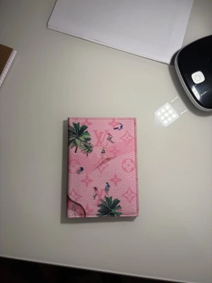 Rosa plånbok  - Snygg rosa plånbok  med tropiskt palmtryck och små figurer. Plånboken har klassiskt -mönster i bakgrunden och är gjord i ett tåligt, strukturerat material. Perfekt för dig som vill ha något unikt och färgglatt i väskan.