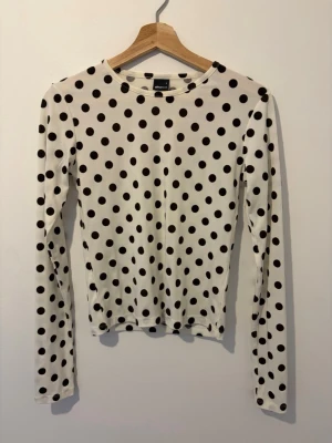 Prickig långärmad topp Gina Tricot - Säljer en vit långärmad topp från Gina Tricot med bruna prickar. Toppen har rund halsringning och är figurnära i modellen. Perfekt för dig som gillar lekfulla mönster och vill sticka ut lite extra.