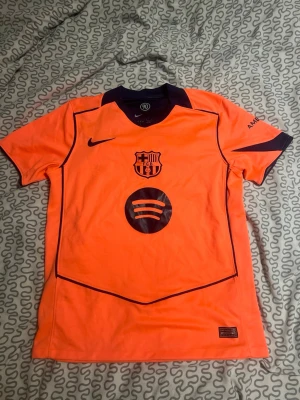 Barcelona orange matchtröja Nike - Snygg orange Barcelona matchtröja från Nike med mörkblå detaljer och klubbmärke på bröstet. Spotify-logga på framsidan och UNHCR-tryck på ryggen. Kortärmad modell i lätt och ventilerande material, perfekt för fotboll eller träning.