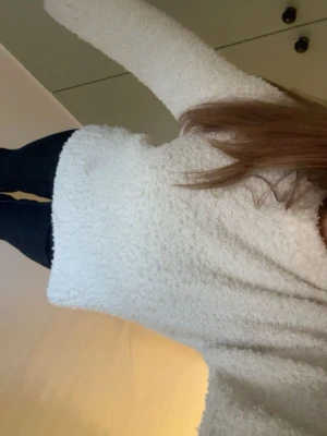 Vit fluffig stickad tröja - Mysig vit stickad tröja med fluffig struktur och långa ärmar. Tröjan har en avslappnad passform och ribbstickade muddar vid ärmslut och nederkant. Perfekt för kalla dagar när du vill vara både varm och snygg.