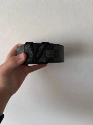Bälte  - Snyggt svart bälte med rutigt mönster och still i metall framtill. Bältet är gjort i skinn och har en stilren design som sticker ut. Perfekt accessoar för att lyfta din outfit.