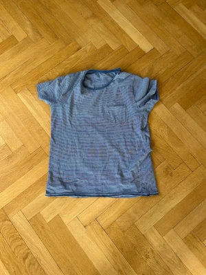 Blåvit randig t-shirt Dressmann - Säljer en blåvit randig t-shirt från Dressmann i storlek XL. T-shirten har korta ärmar, rund halsringning och en liten bröstficka. Tillverkad i mjuk bomull som känns skön mot huden. Perfekt för en avslappnad och enkel stil.