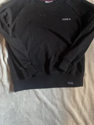 Svart sweatshirt från Marine Sports - En svart sweatshirt från Marine Sports med diskret logga broderad på bröstet. Tröjan har rund halsringning, långa ärmar och ribbade muddar vid ärmslut och nederkant. Perfekt för en avslappnad och sportig stil.