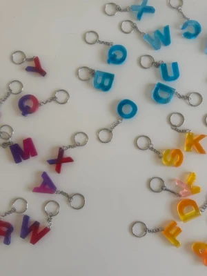 Nyckelringar med bokstavsberlocker - Färgglada nyckelringar med bokstavsberlocker i resin. Finns i flera färger som blå, gul, orange, lila, rosa och röd. Perfekt accessoar för att göra din väska eller nyckelknippa mer personlig och unik.