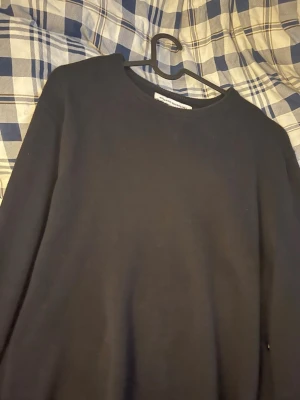 Svart basic långärmad tröja - En enkel svart långärmad tröja med rund halsringning. Perfekt att matcha med jeans eller kjol för en clean och stilren look. Tröjan har en klassisk passform och är ett måste i garderoben.
