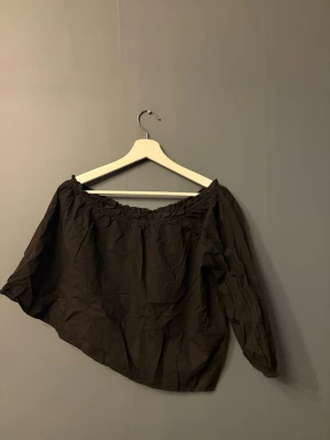 Svart offshoulder blus - Svart blus med offshoulder-modell och långa ärmar. Toppen har en lös passform och resår vid halsringningen för att sitta snyggt över axlarna. 
