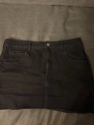Svart jeanskjol med fickor - Snygg svart kort jeanskjol med klassiska fem fickor och bälteshällor. 