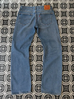 Levis 527 bot cut - Ett par klassiska blå jeans från Levi's med bot cut passform och fem fickor. Jeansen har en ljus tvätt och tydliga sömmar, samt den ikoniska läderpatchen bak i midjan. Perfekta för en avslappnad och tidlös stil.