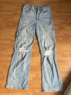 Ljusblå wide jeans med hål - Säljer ett par ljusblå jeans med wide passform och slitningar på båda knäna. Jeansen har hög midja och är gjorda i denim. Mycket bra skick och enkla att styla!
