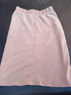 Beige stickad kjol med slits - Mysig beige stickad kjol med rak passform och bred resår i midjan. Kjolen har en enkel design med en snygg slits bak som ger extra rörelsefrihet. Perfekt att matcha med en stickad tröja eller boots för en trendig vinterlook.