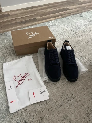 Mörkblå sneakers från Louboutin - Snygga mörkblå sneakers från Louboutin i mocka med klassisk låg siluett och matchande mörkblå snörning. Skorna har en stilren design och beige innersula, perfekta för dig som vill ha något exklusivt och trendigt.