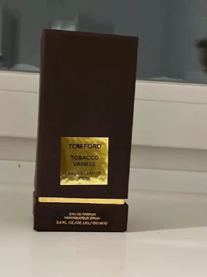 Tom Ford Tobacco Vanille EdP 100 ml - Tom Ford Tobacco Vanille Eau de Parfum 100 ml är en lyxig parfym i en elegant, mörkbrun flaska med gulddetaljer. Doften kombinerar varma toner av tobak och vanilj för en sofistikerad och unik signatur. Flaskan har en stilren, fyrkantig form och känns exklusiv.