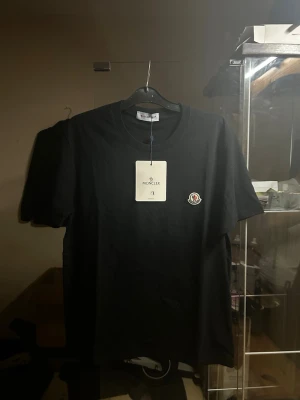 Svart Moncler t-shirt - Snygg svart t-shirt från Moncler med klassisk rund hals och Moncler-logga på bröstet. Tillverkad i mjuk bomull och har en enkel, stilren design som passar perfekt till jeans eller shorts.