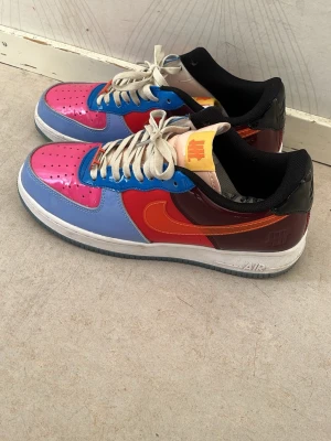 Färgglada låga sneakers i läder - Säljer ett par riktigt färgstarka sneakers med rosa, blå, röd och orange paneler samt vita skosnören. Skorna har en klassisk låg siluett och är tillverkade i glansigt lädermaterial. Perfekta för dig som vill sticka ut med din stil.