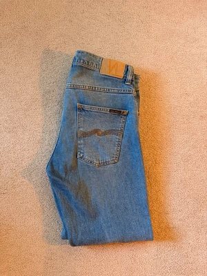 Nudie Jeans - Grim Tim  - Nudie Jeans i ljusblå färg, modellen är Grim Tim - True Gold. Lite uppsydda.   Nypris 1600kr.   Jeans mått: Midja: 41cm kant till kant Innermått ben: 71cm Yttermått ben: 100cm 