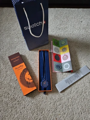 AP X Swatch Orenji Hachi RoyalPop klocka - Snygg blå klocka från Audemars Piguet x Swatch, modell Orenji Hachi RoyalPop. Klockan har en rund urtavla med orange detaljer och blått armband. Levereras i originalförpackning med tillhörande påse och manual. Perfekt accessoar för dig som vill sticka ut med färg och stil.