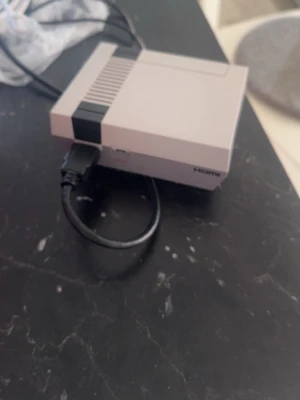 Nintendo Classic Mini NES konsol - Säljer en Nintendo Classic Mini NES konsol i grått med svart detalj. Konsolen har två portar för handkontroller och HDMI-utgång. Den klassiska retrodesignen är kompakt och perfekt för nostalgiska spelkvällar. Tillverkad i plast. Saknas strömkabel! 
